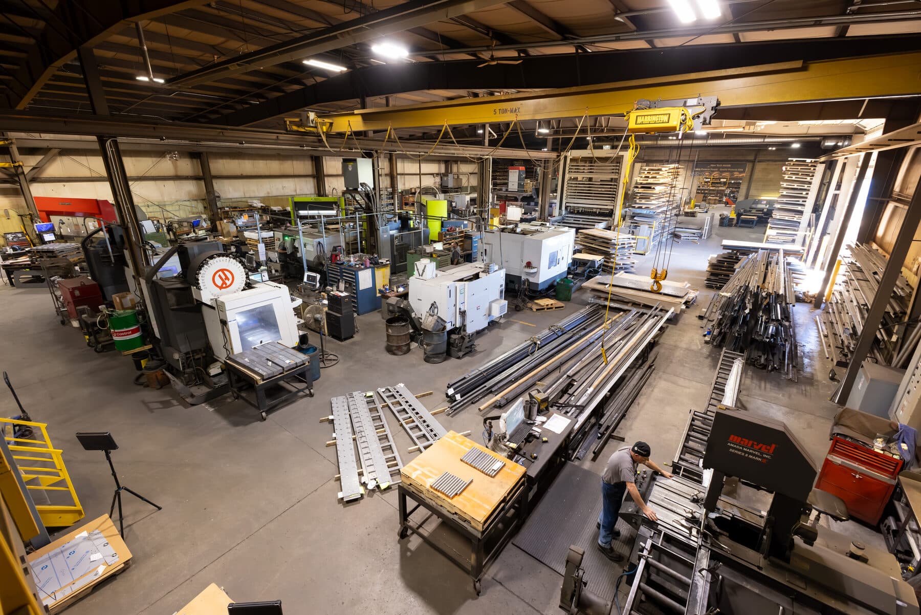 New Tech Metals machine shop floor: CNC machining centers, a 5-ton overhead crane, press brakes, and raw steel bar stock in New Franken, Wisconsin